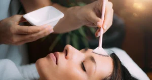Woman receiving a VI Peel in Kentfield, CA facial treatment; a technician applies product to her forehead with a pink fan brush.